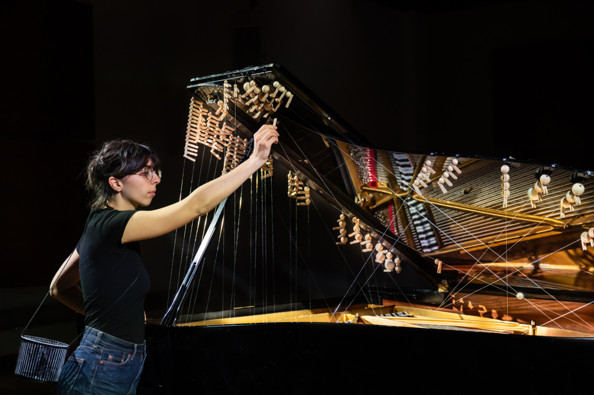 Carmel Curiel montiert eine Wäscheklammer aus Holz an Fäden, die in einem geöffneten Flügel gespannt sind, die bereits einige Wäscheklammern und Kugeln tragen