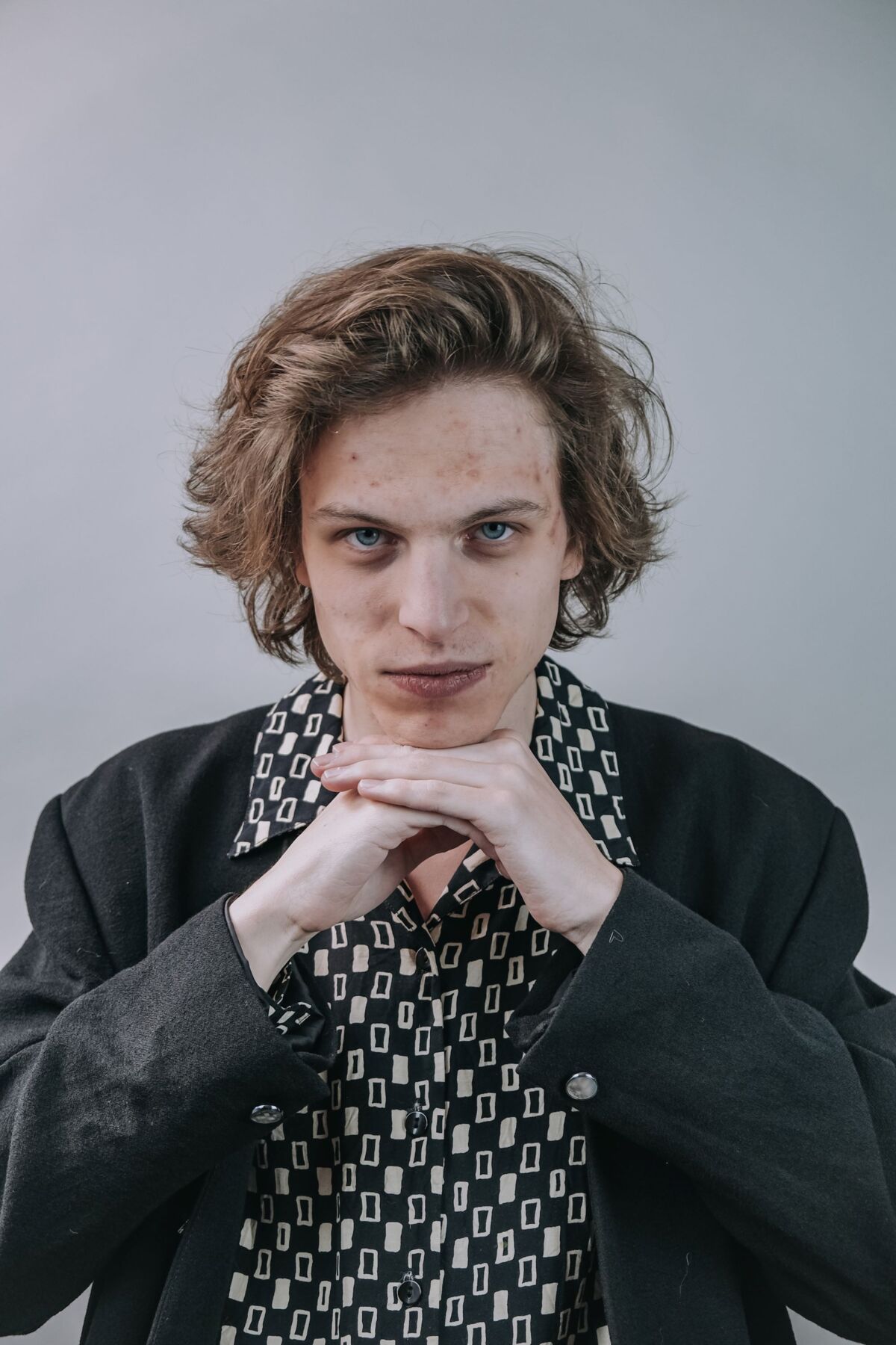 Portrait von Vili Polajnar, der vor grauem Hintergrund in schwarzem Jackett und gemustertem Hemd sein Kinn auf seinen Händen abstützt und frech in die Kamera schaut