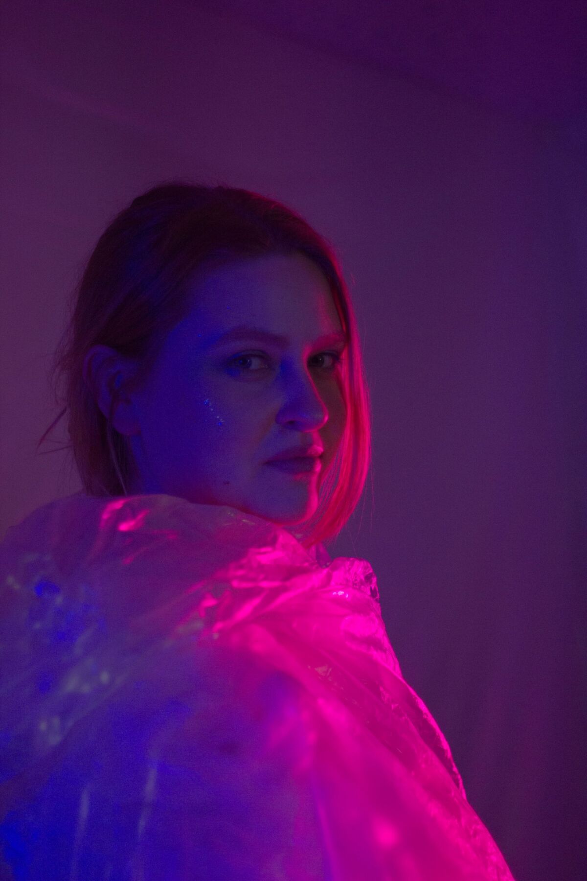 Barbora Jirásková schaut schräg über die Schulter zu uns, trägt einen Regenmantel aus Plastik, der pink-blaues Licht reflektiert
