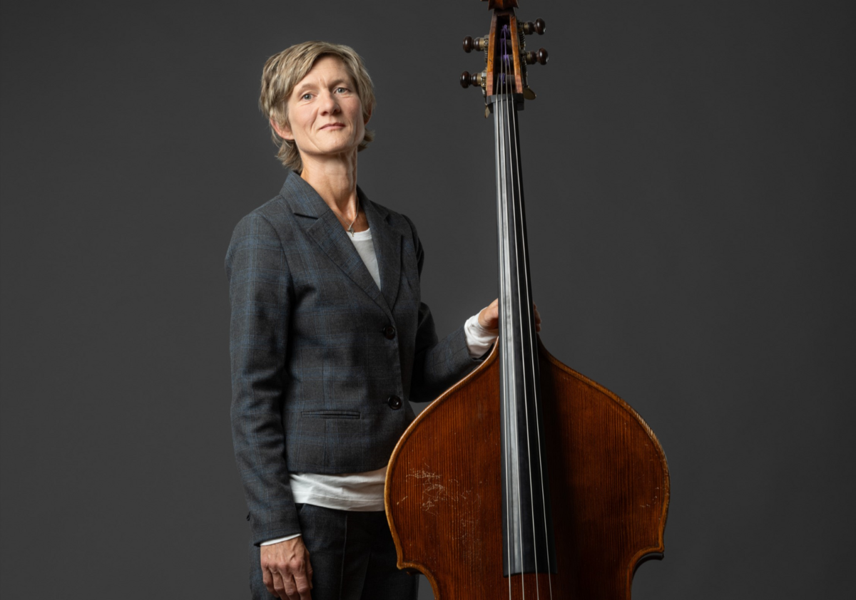 Foto von Eva Kruse vor dunkelgrauem Hintergrund, die stolz ihren Kontrabass hält
