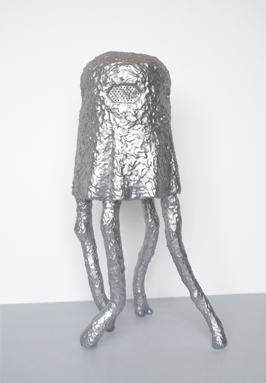Eines ihrer silbrigen Wesen, die aussehen wie in Aluminium eingewickelte Schaumküsse auf vier Beinen, steht allein vor einer weissen Wand.