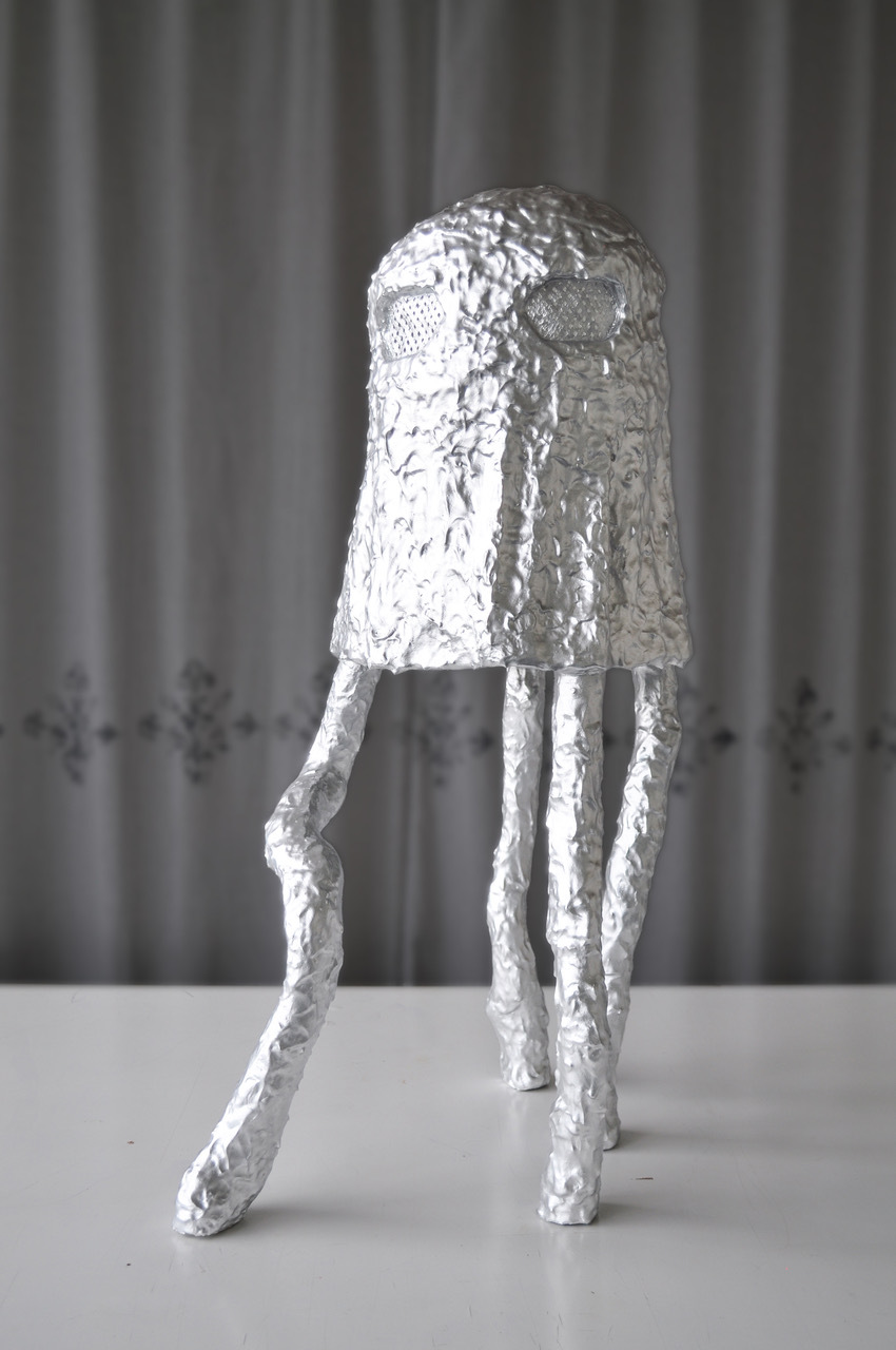 Eines ihrer silbrigen Wesen, die aussehen wie in Aluminium eingewickelte Schaumküsse auf vier Beinen, steht allein vor einem grauen Vorhang.